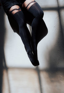 Eine Nahaufname unserer Strumpfhosen, die das Muster oben im Detail zeigen. Von oben fällt Sonnenlicht auf die Beine und den Boden. Das Model trägt schwarze Shorts.